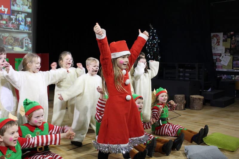 Besiedkové predstavenie školských detí v prezlekoch za Santu, elfov a soby predvádzajúce vianočnú hru