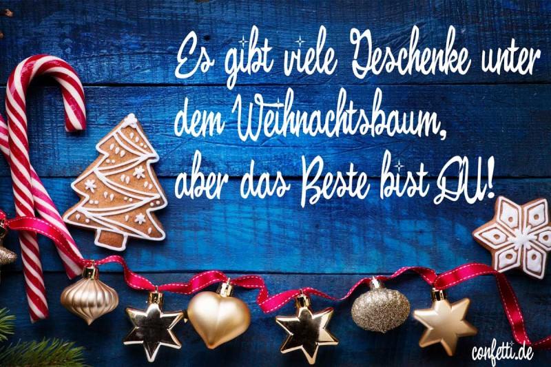 Text vianočného priania v nemčine na modrom dreve, ozdobenom perníkmi, paličkami a ozdobami na červenej stužke