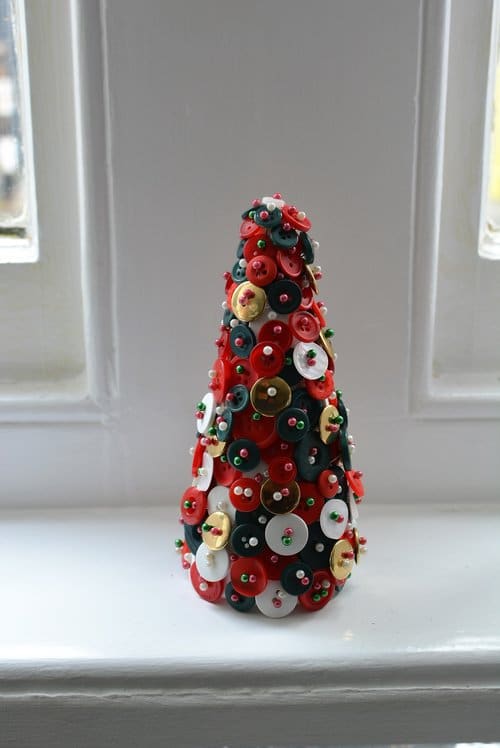 Vianočná výzdoba bytu v tvare stromčeka, vyrobená z farebných gombíkov a špendlíkov.