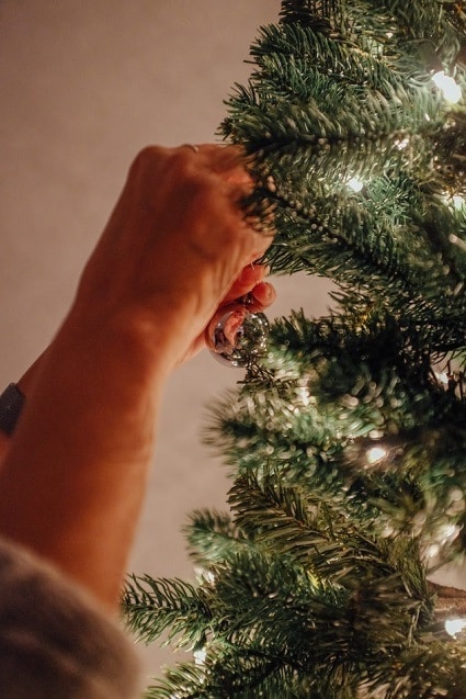 Detail na ruky zdobiaci vianočný stromček so svetielkami.