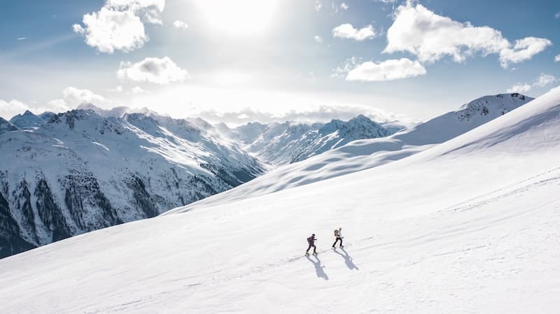 Dvojica kráča k vrcholu zasneženou planinou.