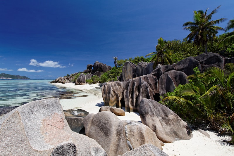 Pláže na Seychelách s bielym pieskom a typickými skaliskami, lemované prírodou s palmami.
